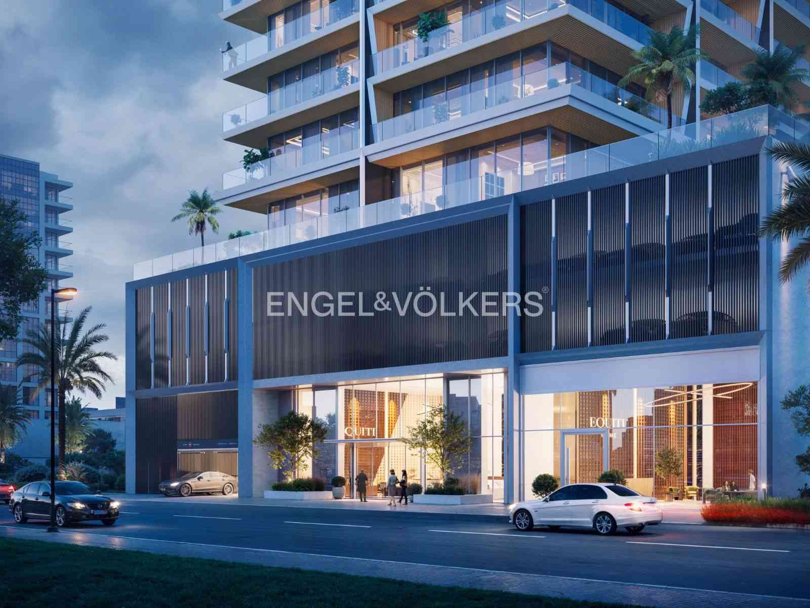Exterior of a modern, multi-story building with the Engel & Völkers logo. Cars are parked outside. Palm trees are visible.