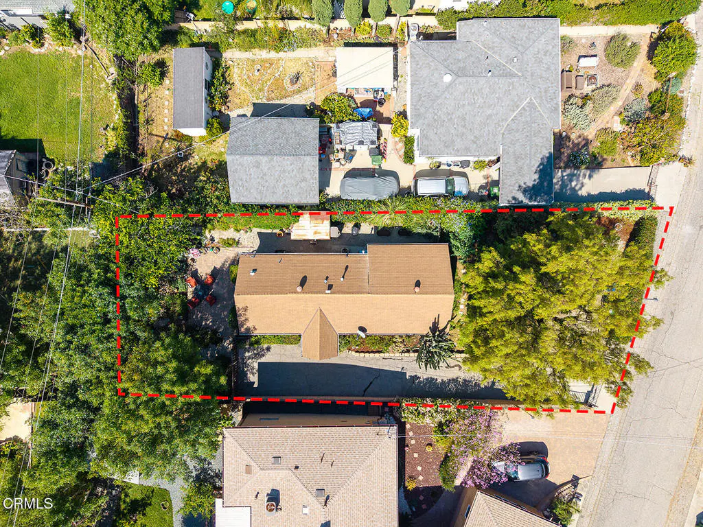 Aerial view of a property with a brown roof, surrounded by green trees and a red dotted line.