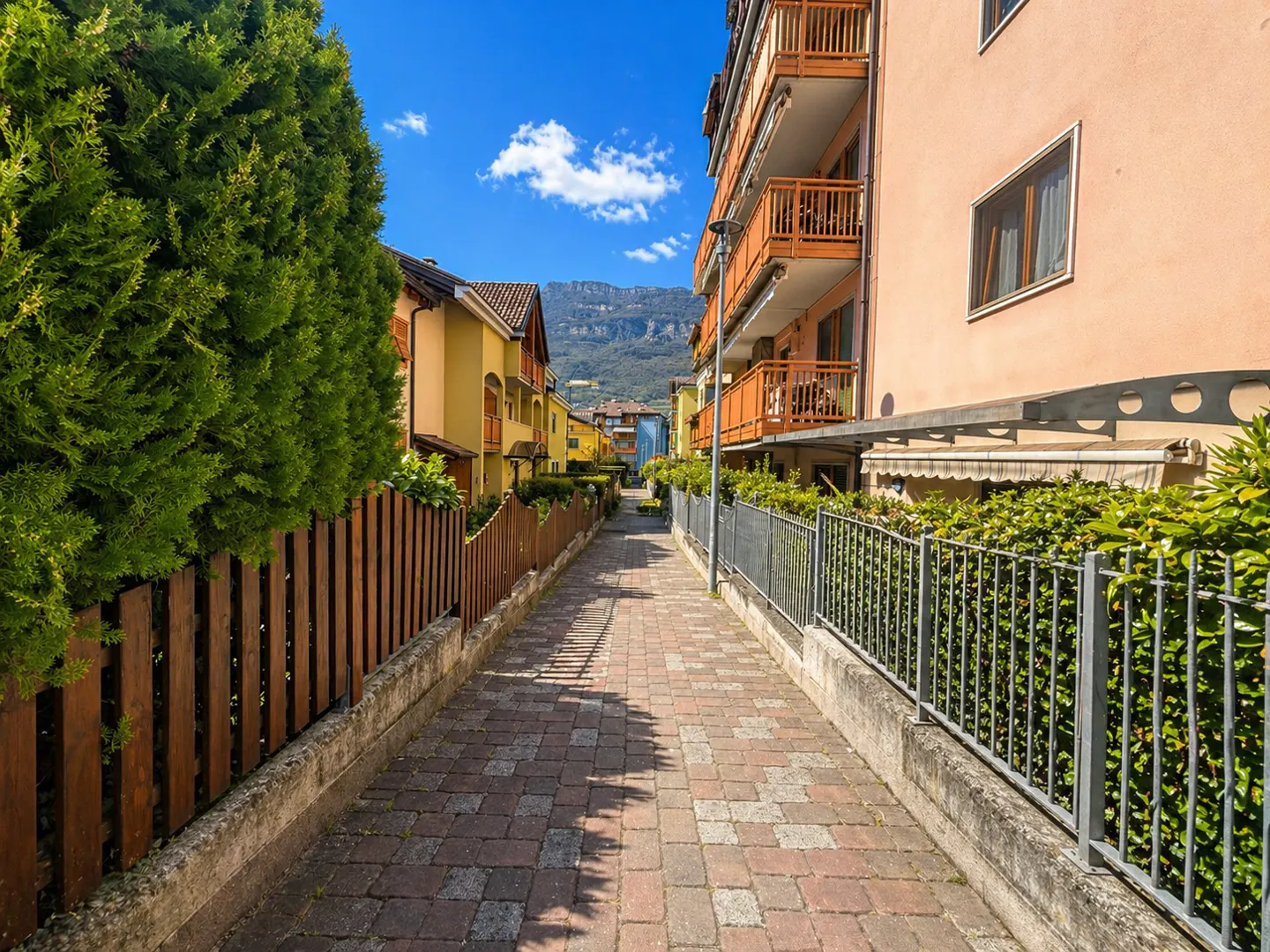 A brick pathway lined with fences and greenery leads to colorful buildings under a blue sky.