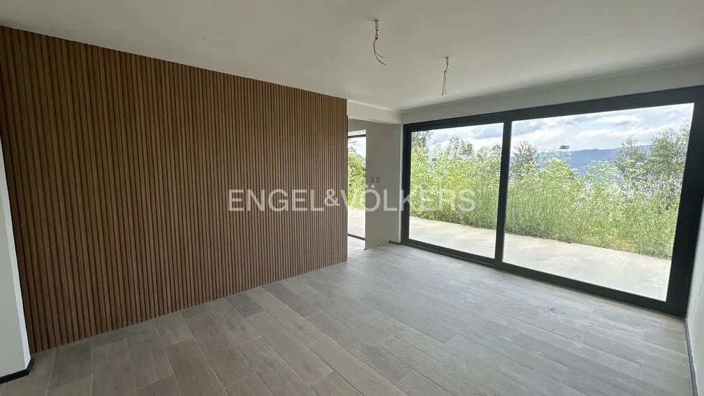An empty room with wood-look tile floors, a wood slat wall, and a large sliding glass door with a view of greenery.
