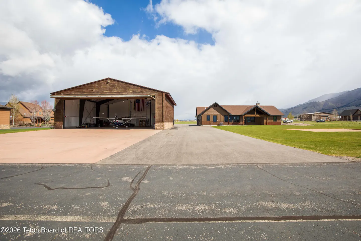 Exterior view of a brown house with an airplane hangar, runway, and green lawn.