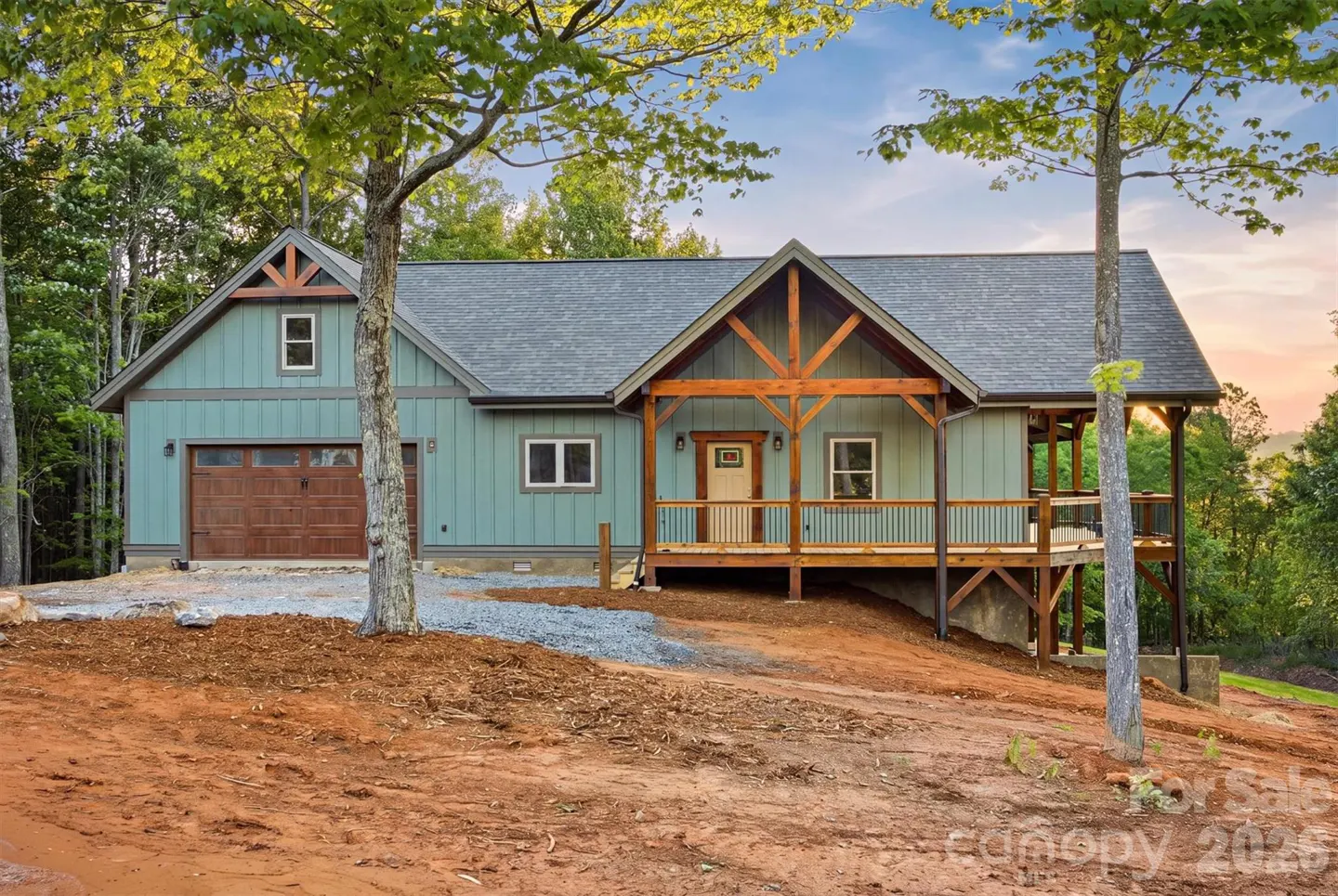 Exterior of a light green house with a brown garage door and wooden porch. The house is surrounded by trees.
