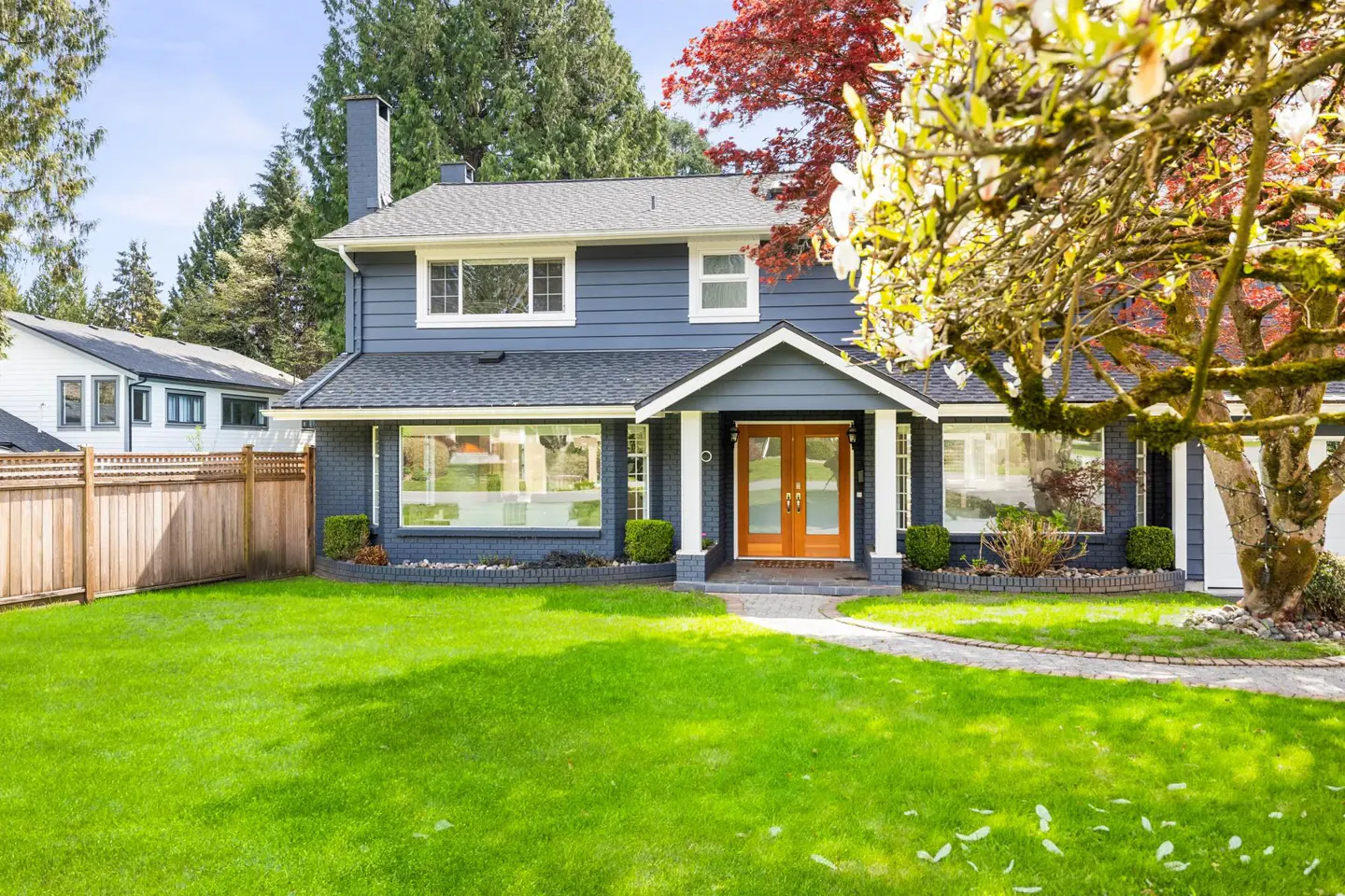 Two-story blue house with a green lawn, a gray roof, and a brown double door.