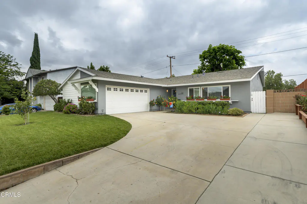 Exterior view of a single-story gray house with a white garage door and a concrete driveway on a cloudy day.