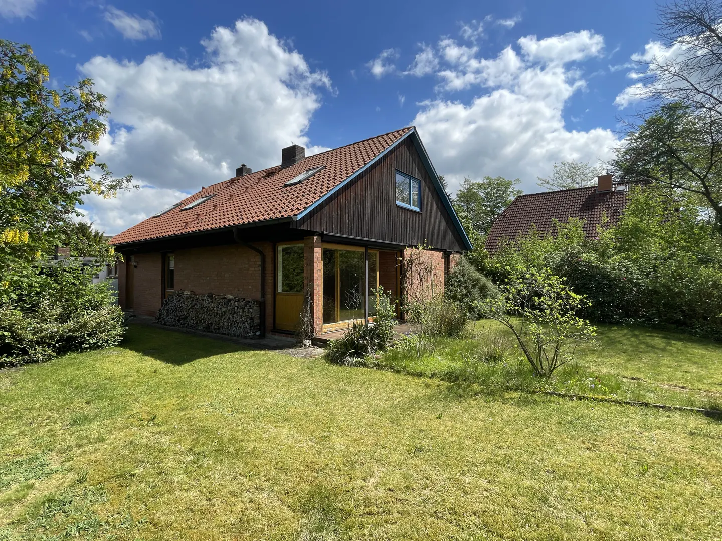 Exterior view of a brick house with a red tile roof, wood siding, and a green lawn under a blue sky with clouds.