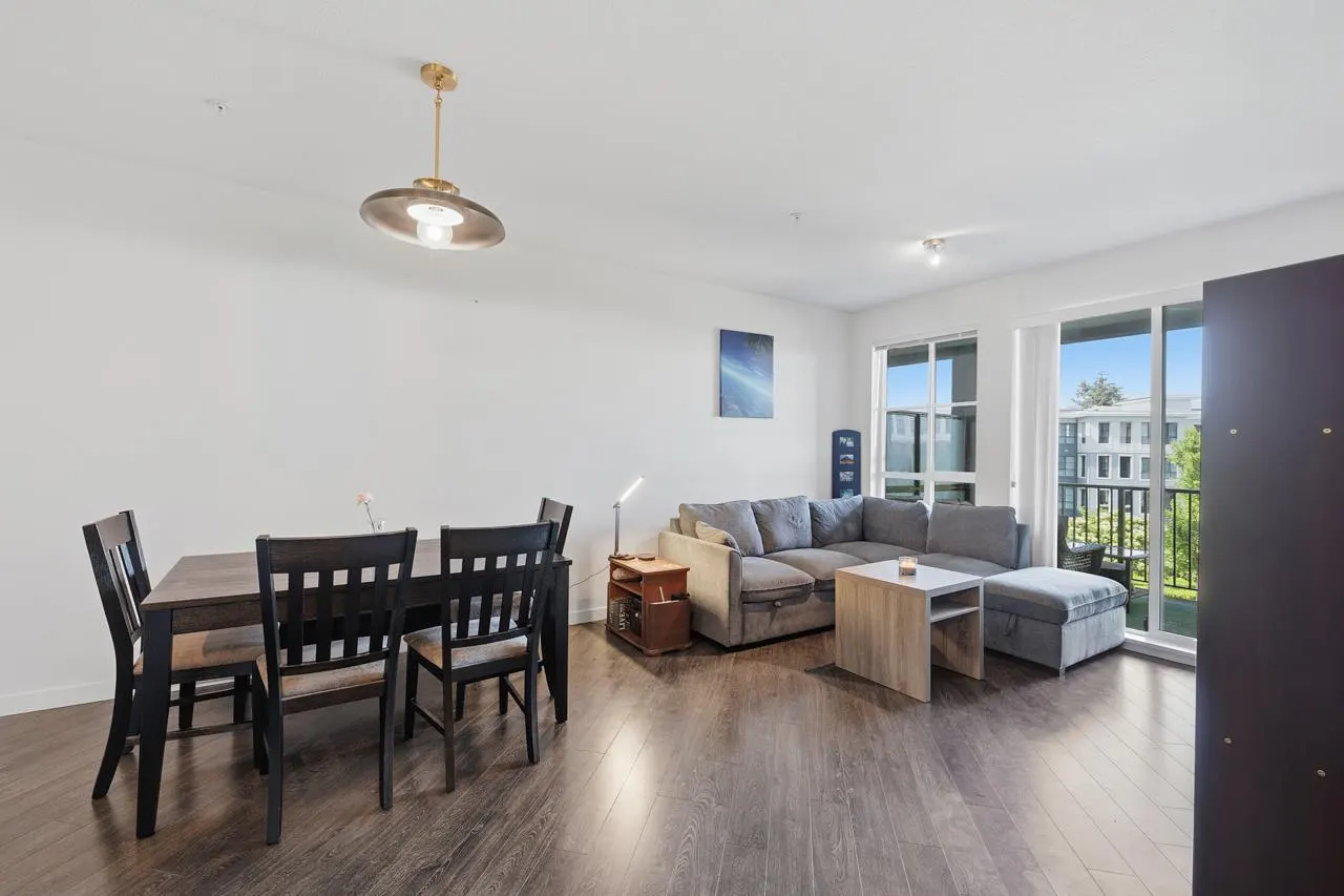 Bright, open-concept living space with dark wood floors, dining table, and gray sectional sofa near a window.