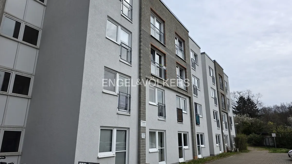 Exterior view of a multi-story apartment building with gray walls, white windows, and small balconies. Engel & Völkers logo visible.
