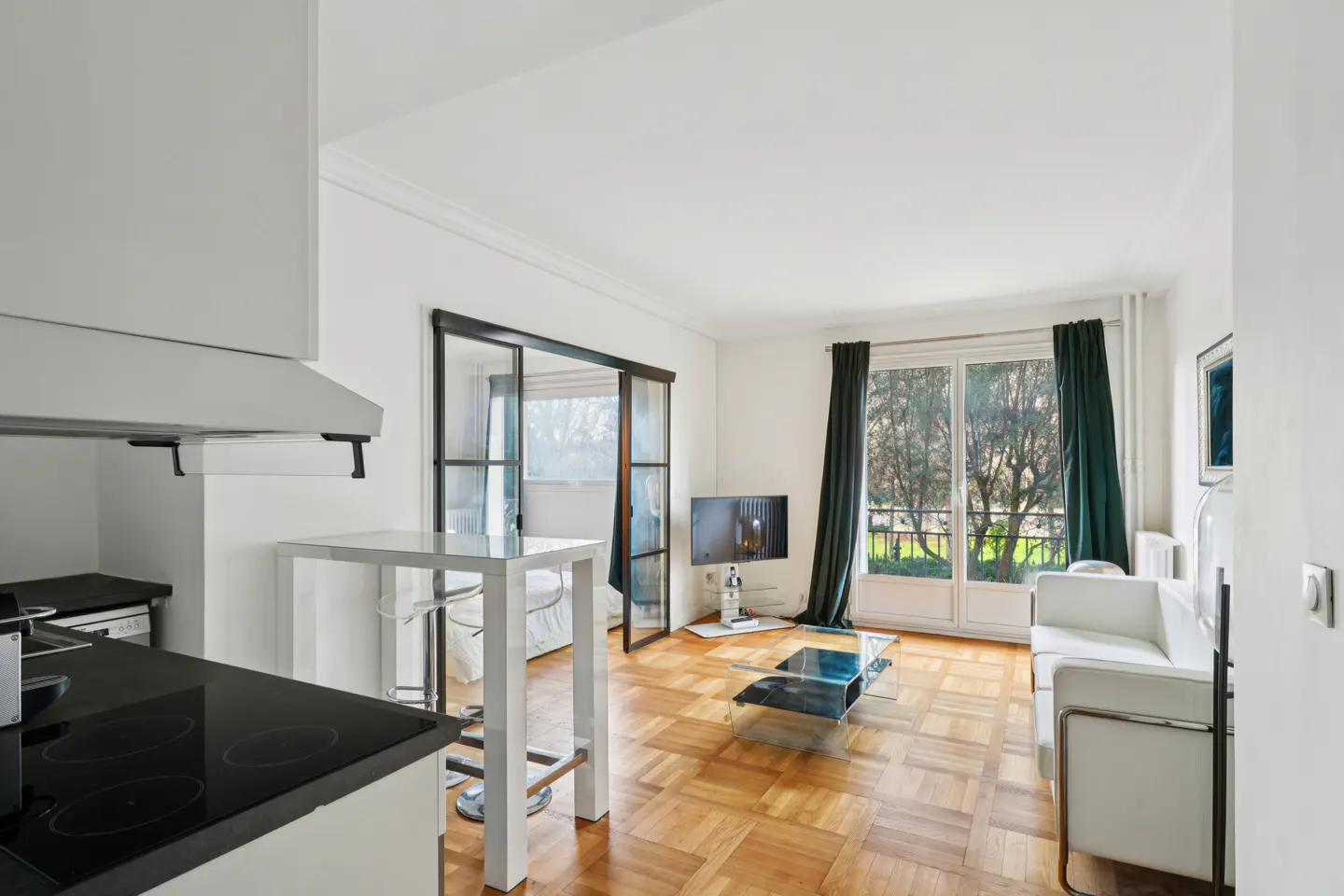 Modern living room with parquet floors, white sofa, glass coffee table, and sliding glass doors leading to a balcony.