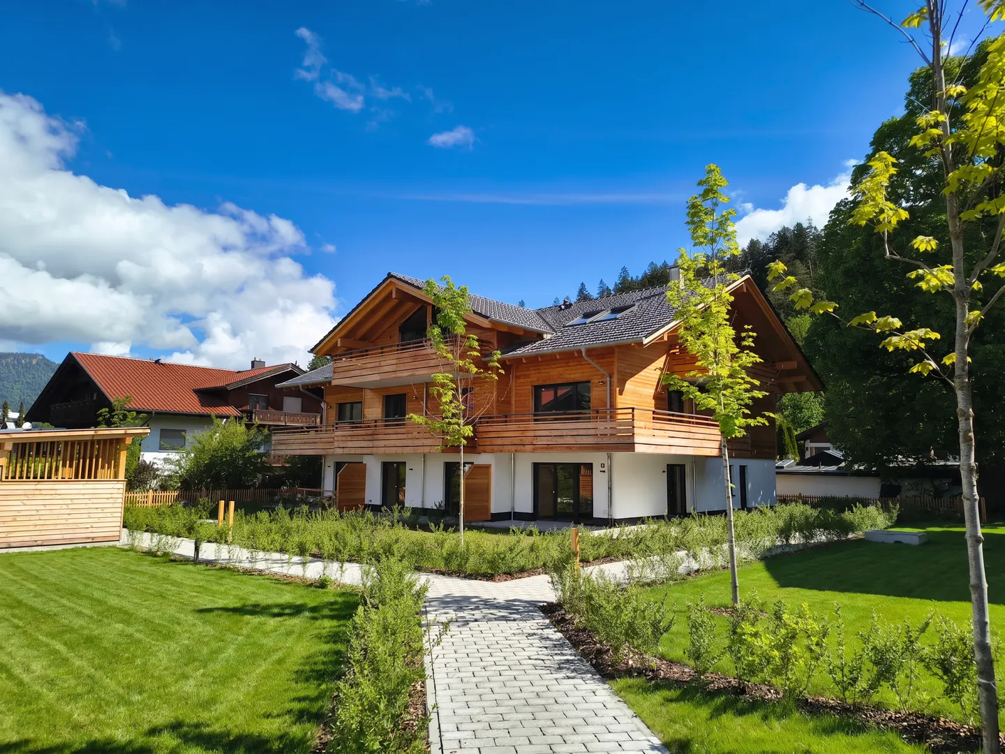Two-story house with wood siding and white foundation, green lawn, stone path, and blue sky with clouds.