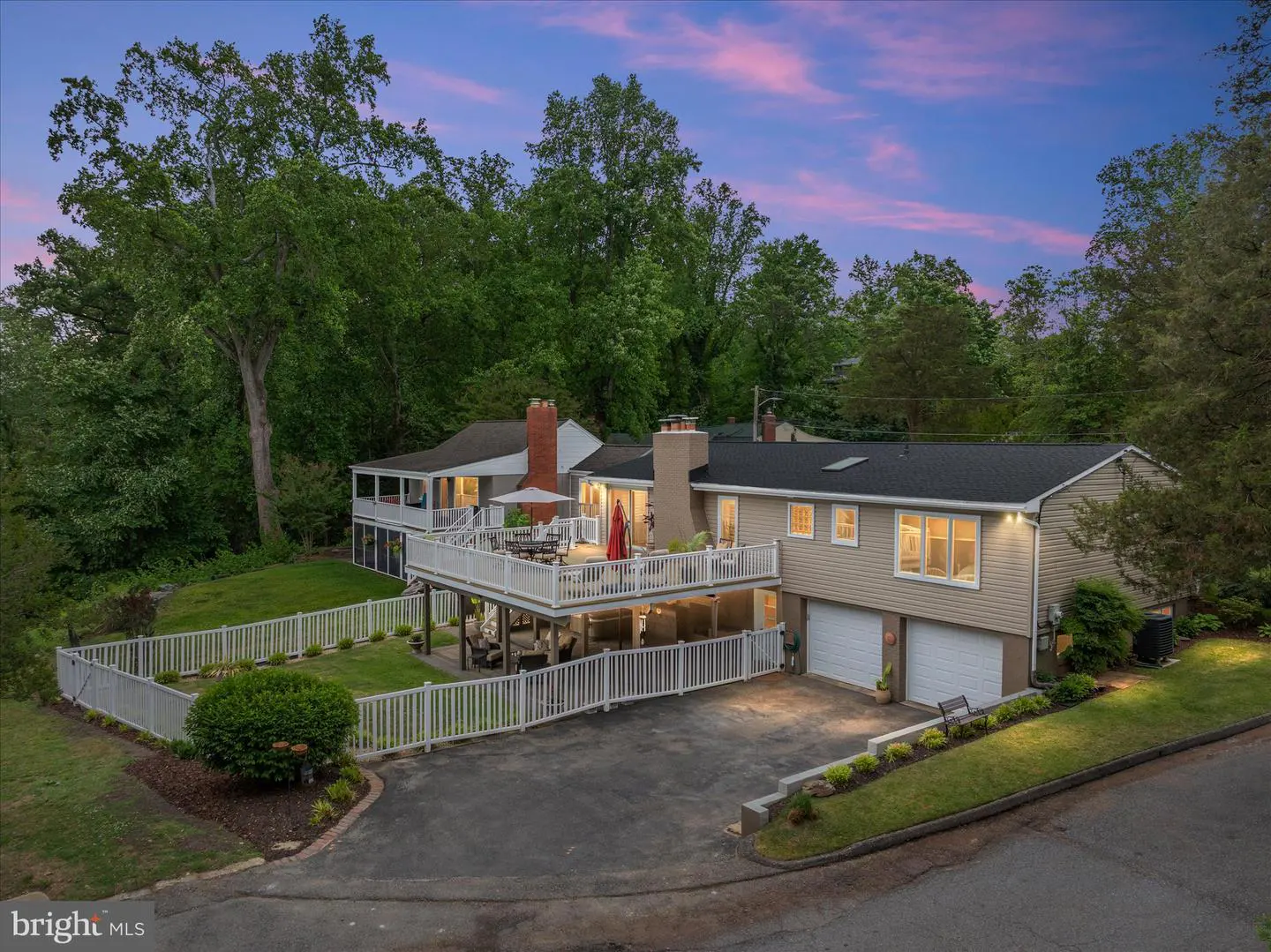 Exterior view of a two-story beige house with a white fence and a large deck at dusk.