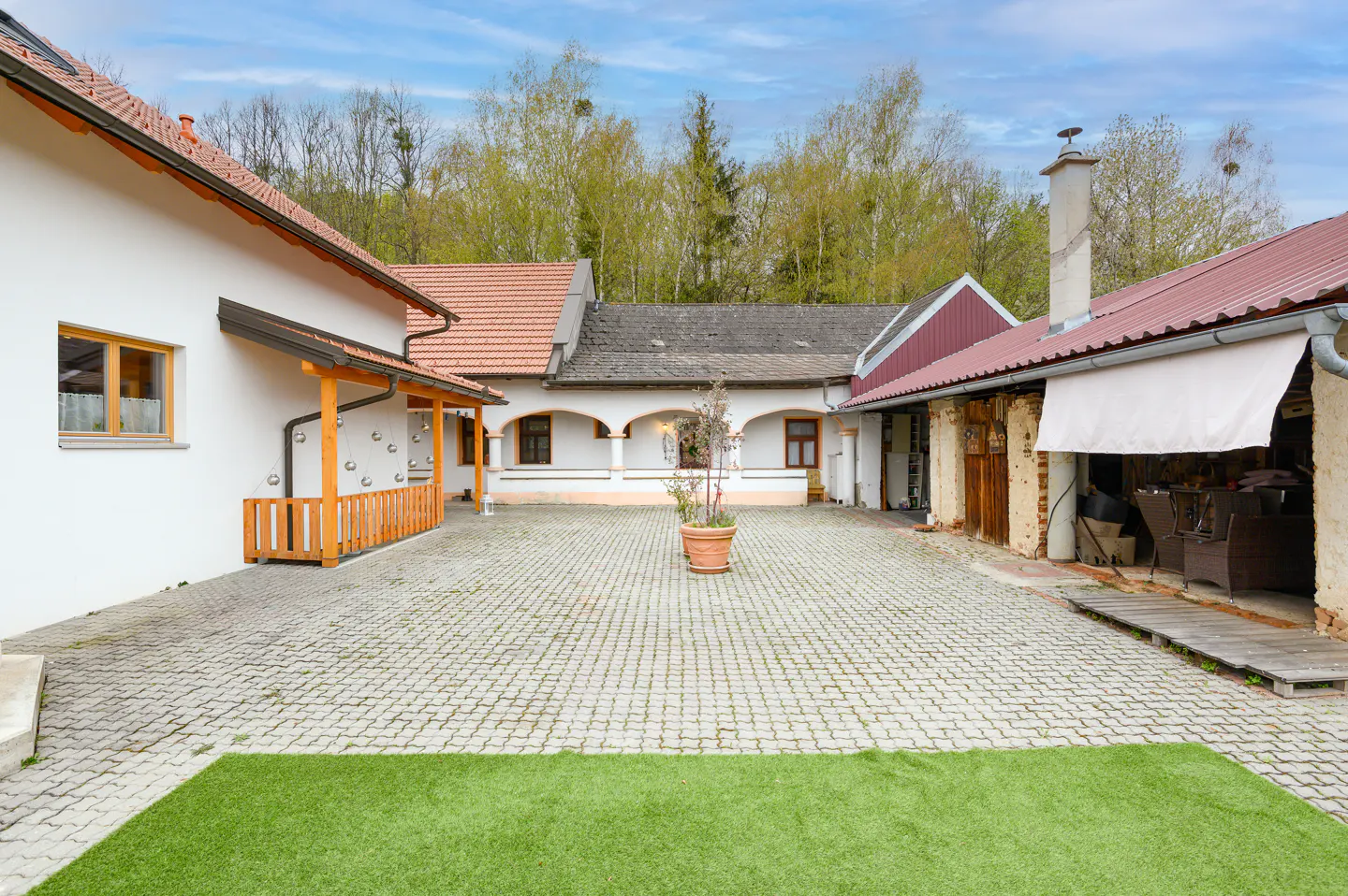 Courtyard view of a white building complex with red roofs and a cobblestone ground. A potted plant sits in the center.