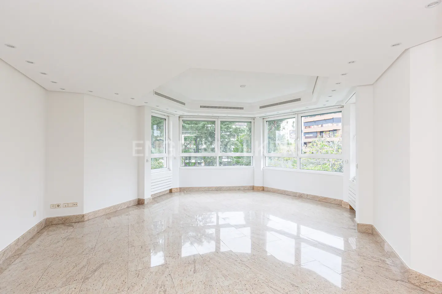 Bright, empty room with white walls, marble floors, and large windows overlooking greenery.