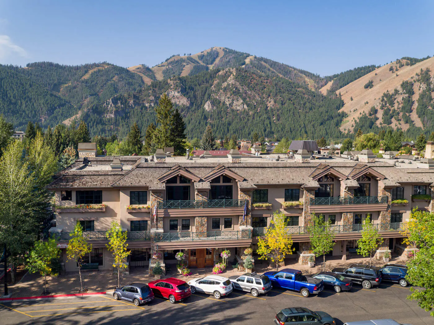 A multi-story building with a stone facade and a mountain backdrop. Cars are parked in front.