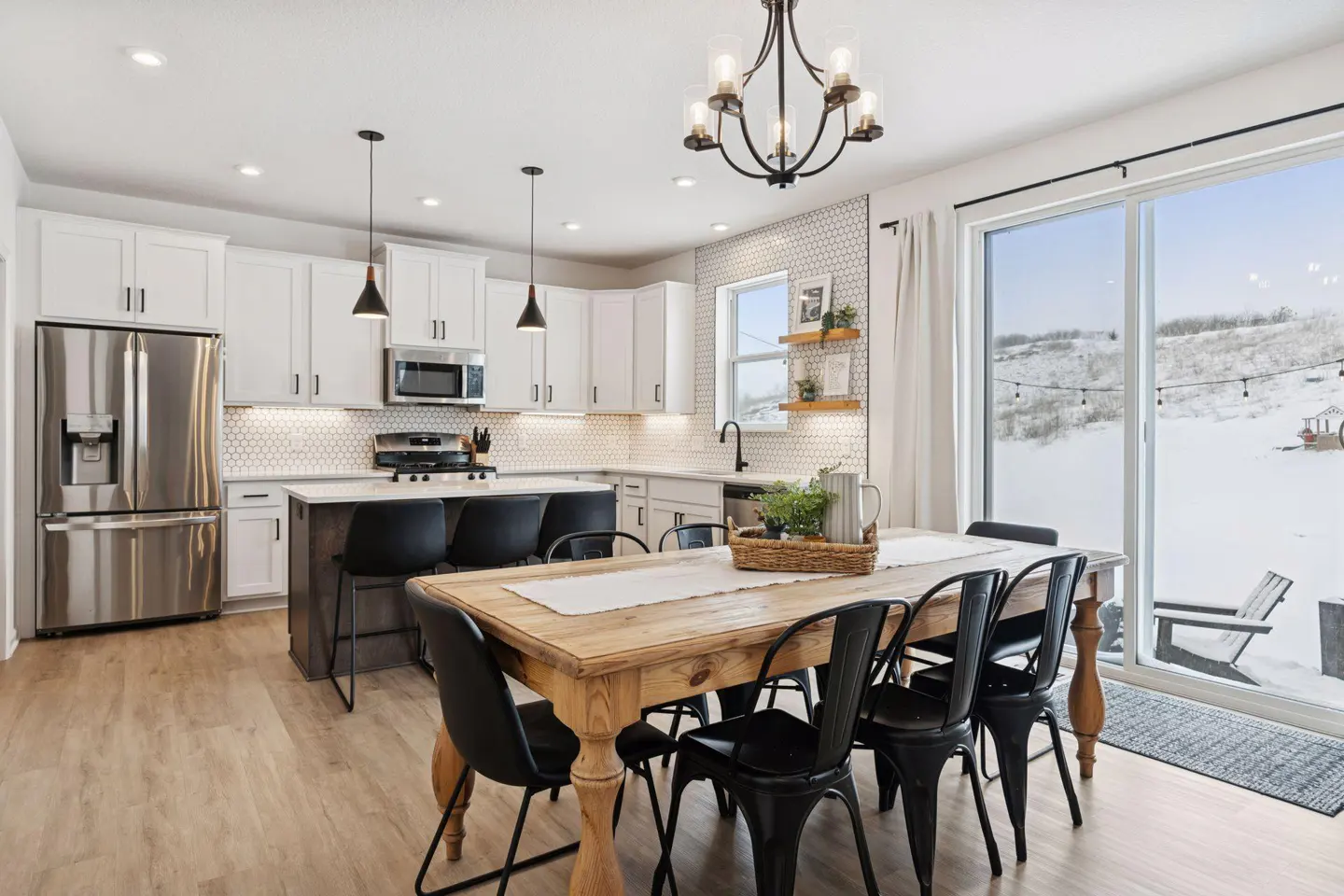 Bright kitchen with white cabinets, black accents, and a wood dining table. A sliding glass door reveals a snowy backyard.