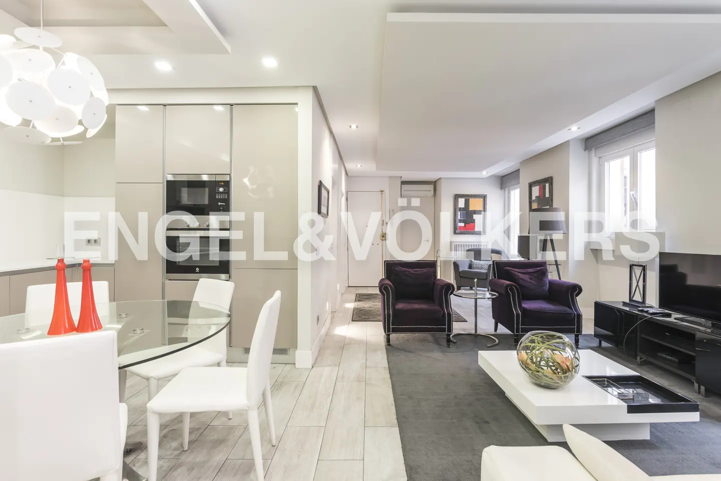 Open-concept living space with kitchen, dining area, and lounge. Features include purple armchairs, white furniture, and modern lighting.