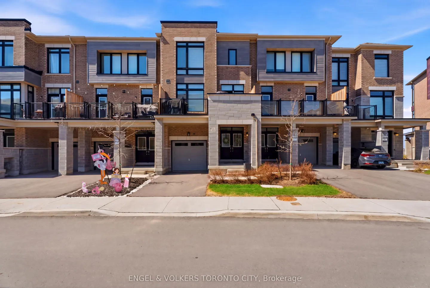 Row of modern townhouses with brick and stone facades, black framed windows, and attached garages on a sunny day.