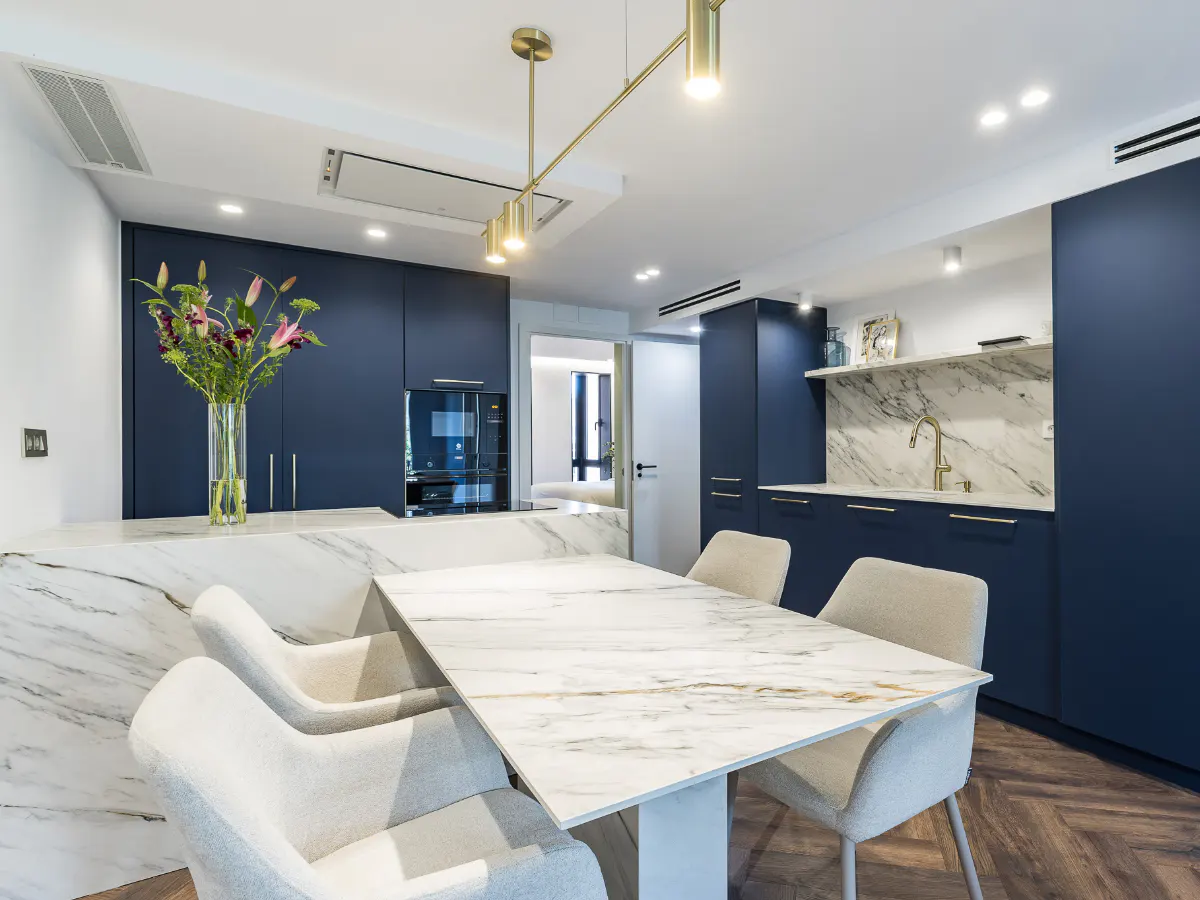 A modern kitchen with blue cabinets, marble countertops, and a dining table with four chairs.