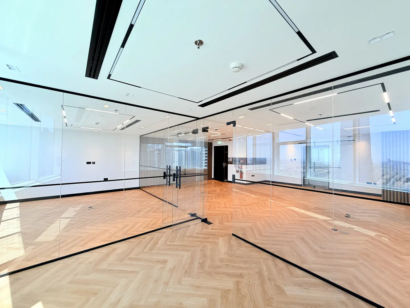 Empty office space with glass walls, herringbone wood floors, and a view of the city.