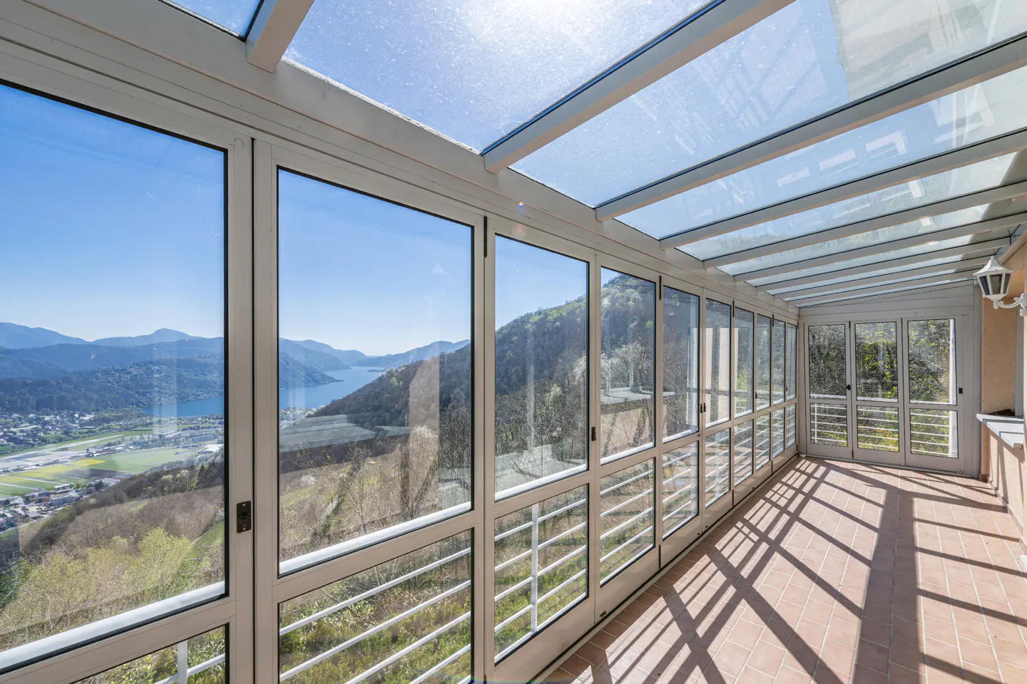 Sunroom with glass ceiling and walls, terracotta tile floor, and mountain view.