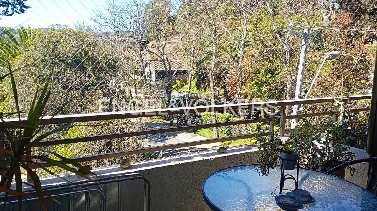 Balcony view with a glass table, plants, and a metal railing overlooking trees and a road. Engel & Volkers logo visible.