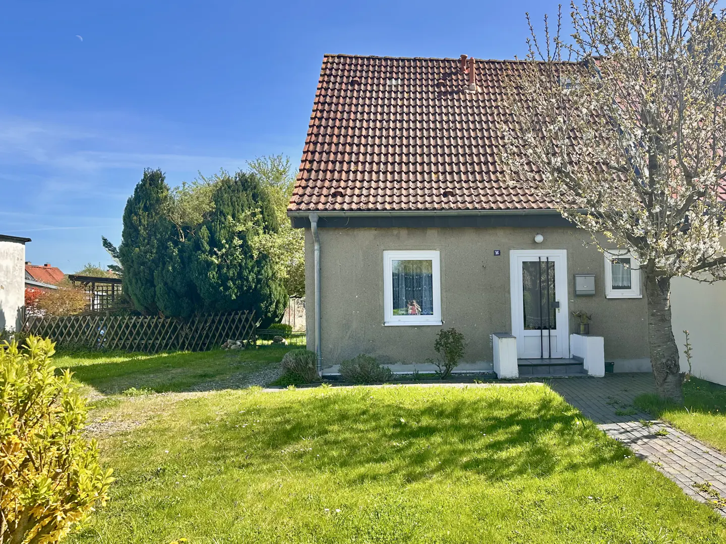 A one-story house with a red tile roof and a green lawn on a sunny day.