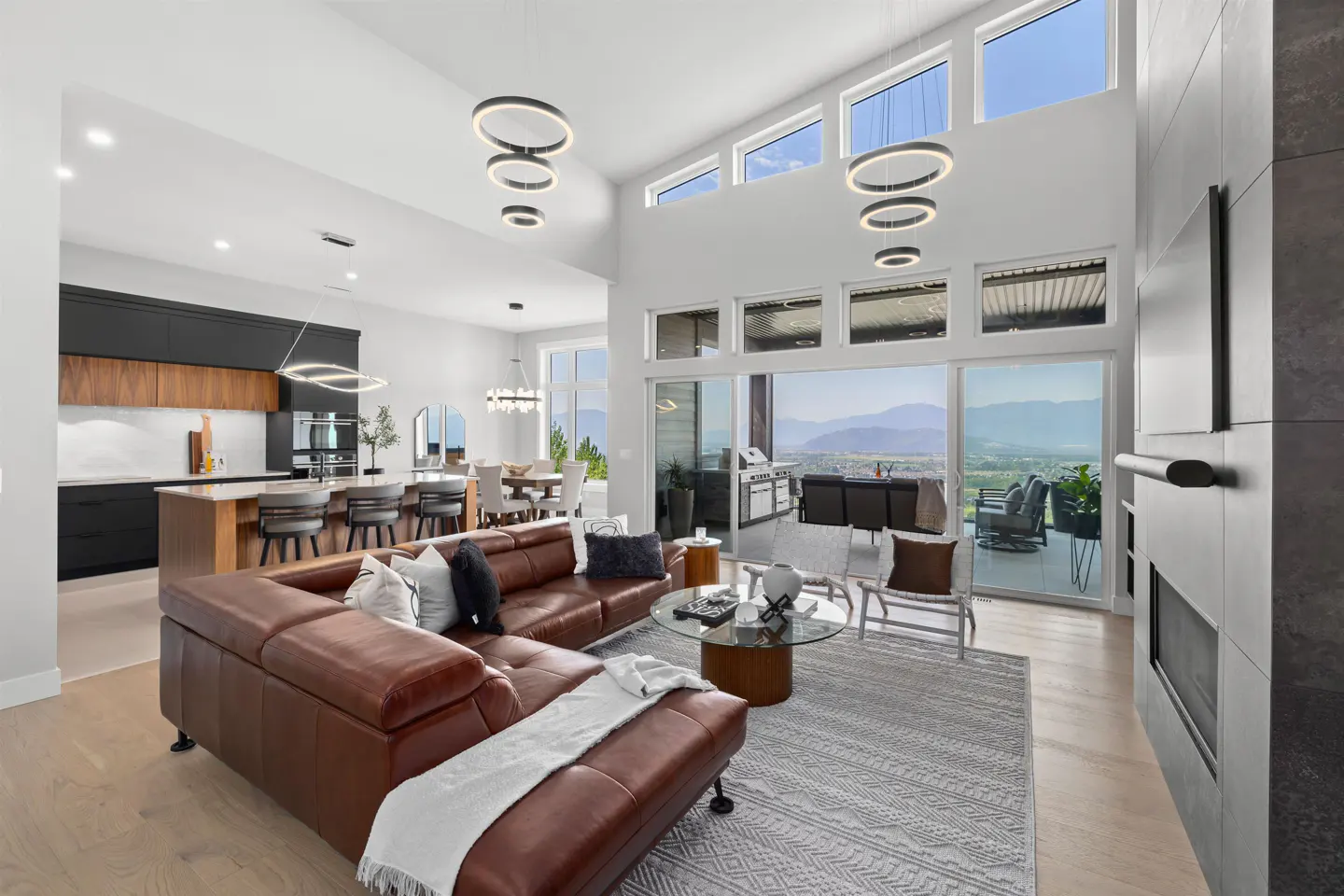 Open-concept living space with brown leather sectional, kitchen island, dining table, and patio with mountain views.