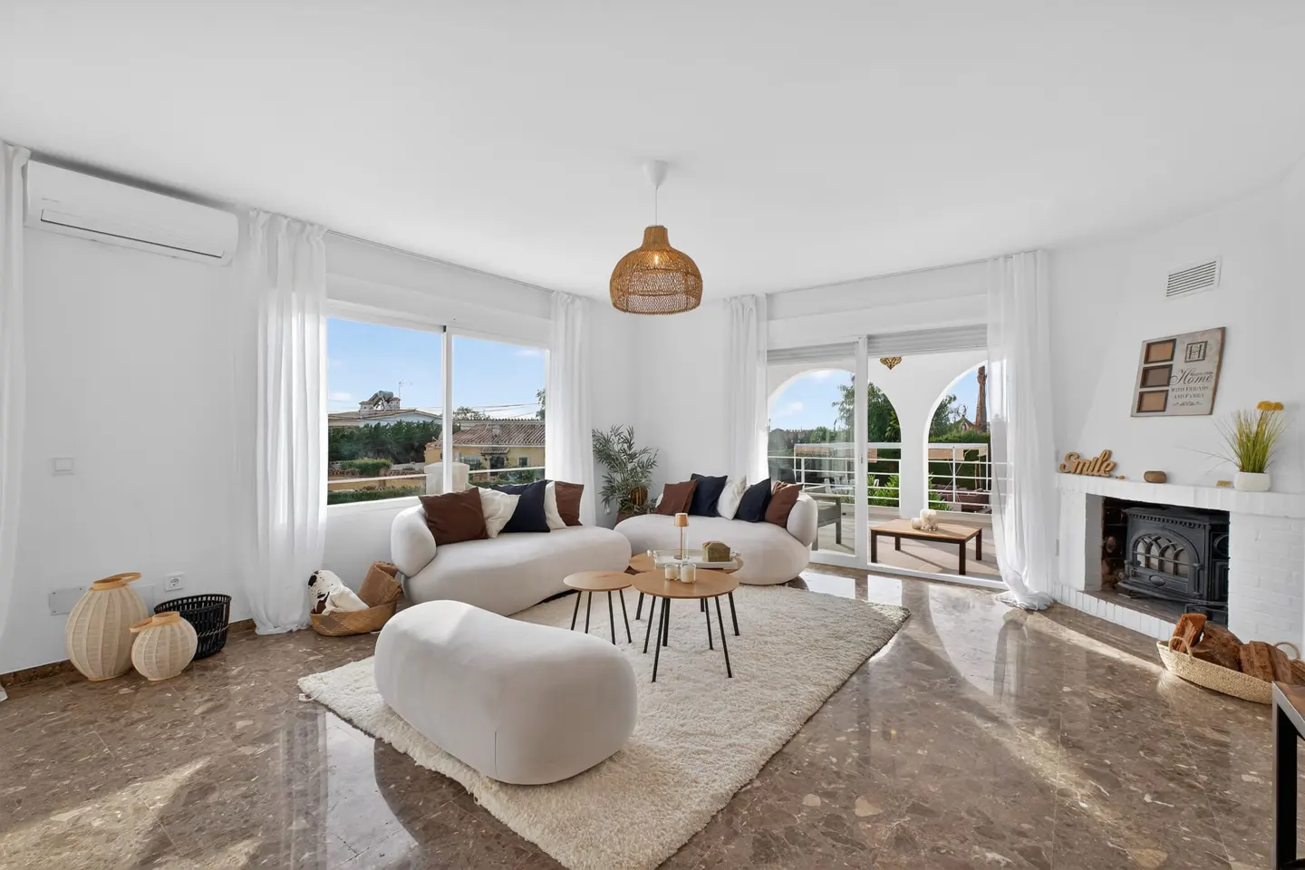 Bright, modern living room with white curved sofas, a textured rug, marble floors, a fireplace, and a balcony view.