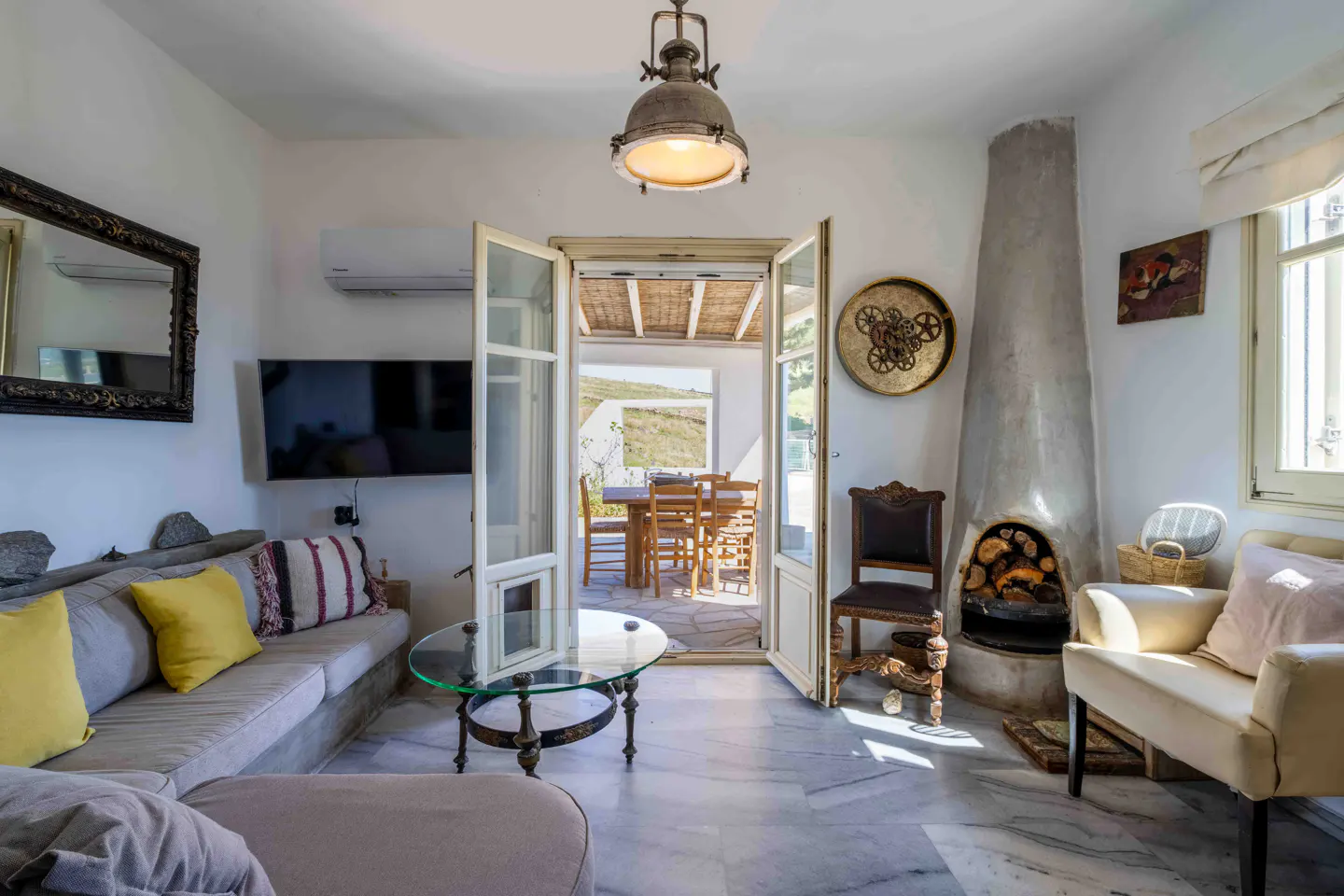 Bright living room with a gray sofa, yellow pillows, a fireplace, and an open door to an outdoor dining area.
