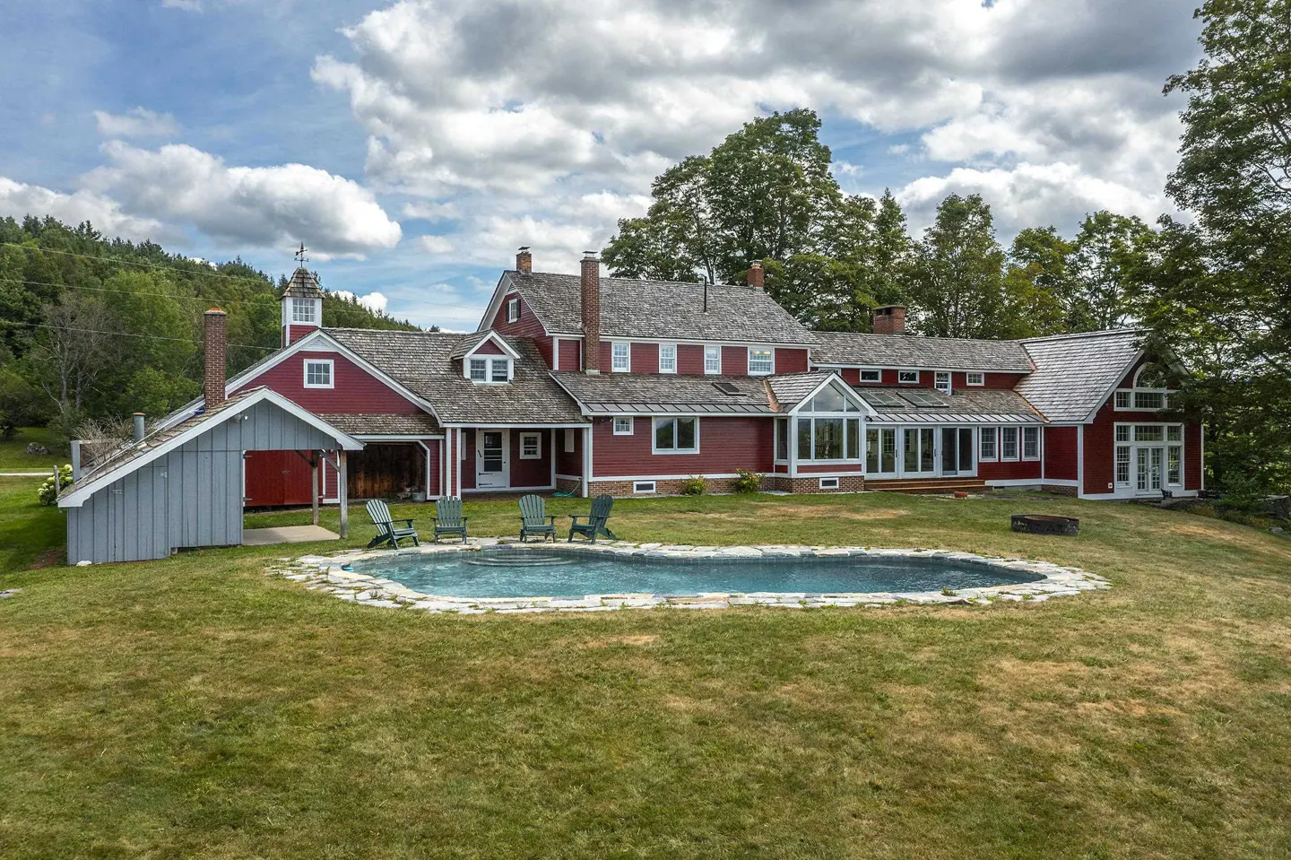 A large red house with a pool and green lawn on a sunny day.