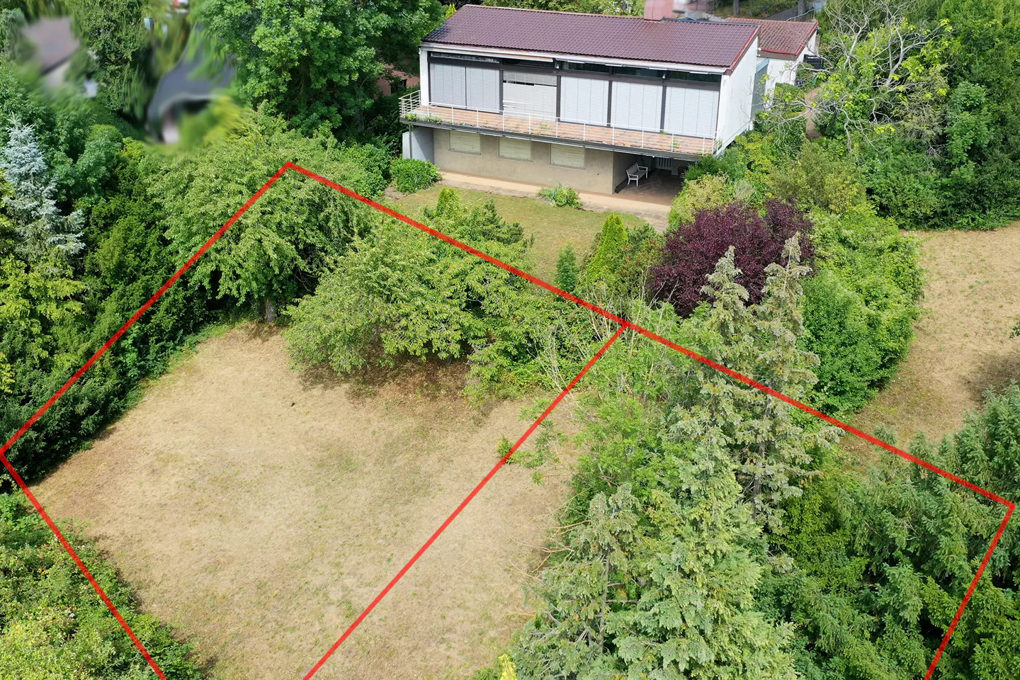 Aerial view of a residential plot outlined in red, featuring a modern two-story house surrounded by lush green trees.