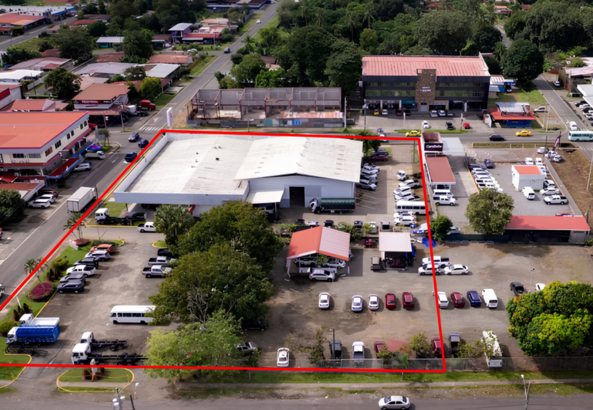 Aerial view of a commercial property outlined in red, featuring a large warehouse, parking lot, and surrounding city streets.