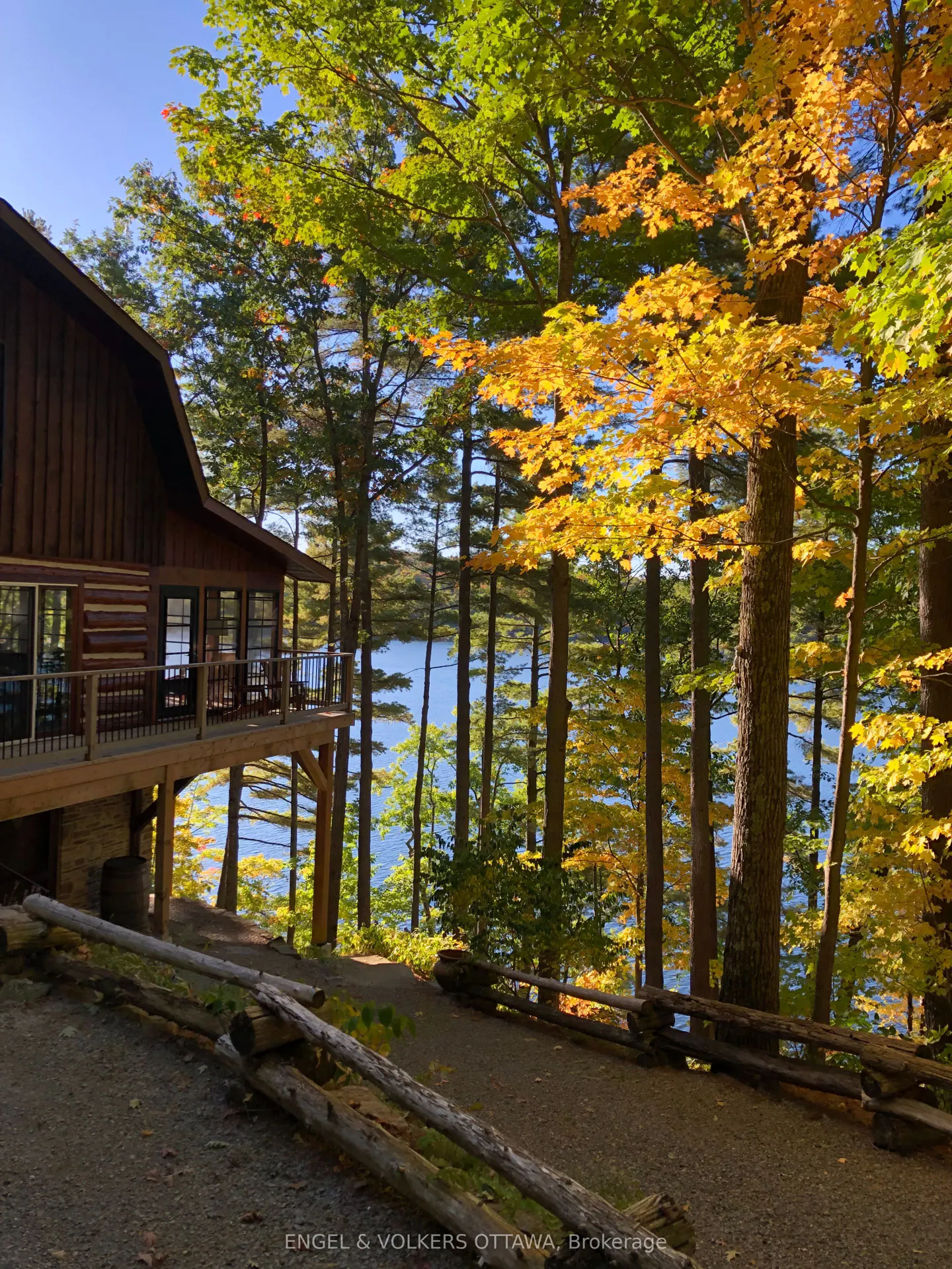 Log cabin with a deck overlooking a lake surrounded by trees with autumn foliage.