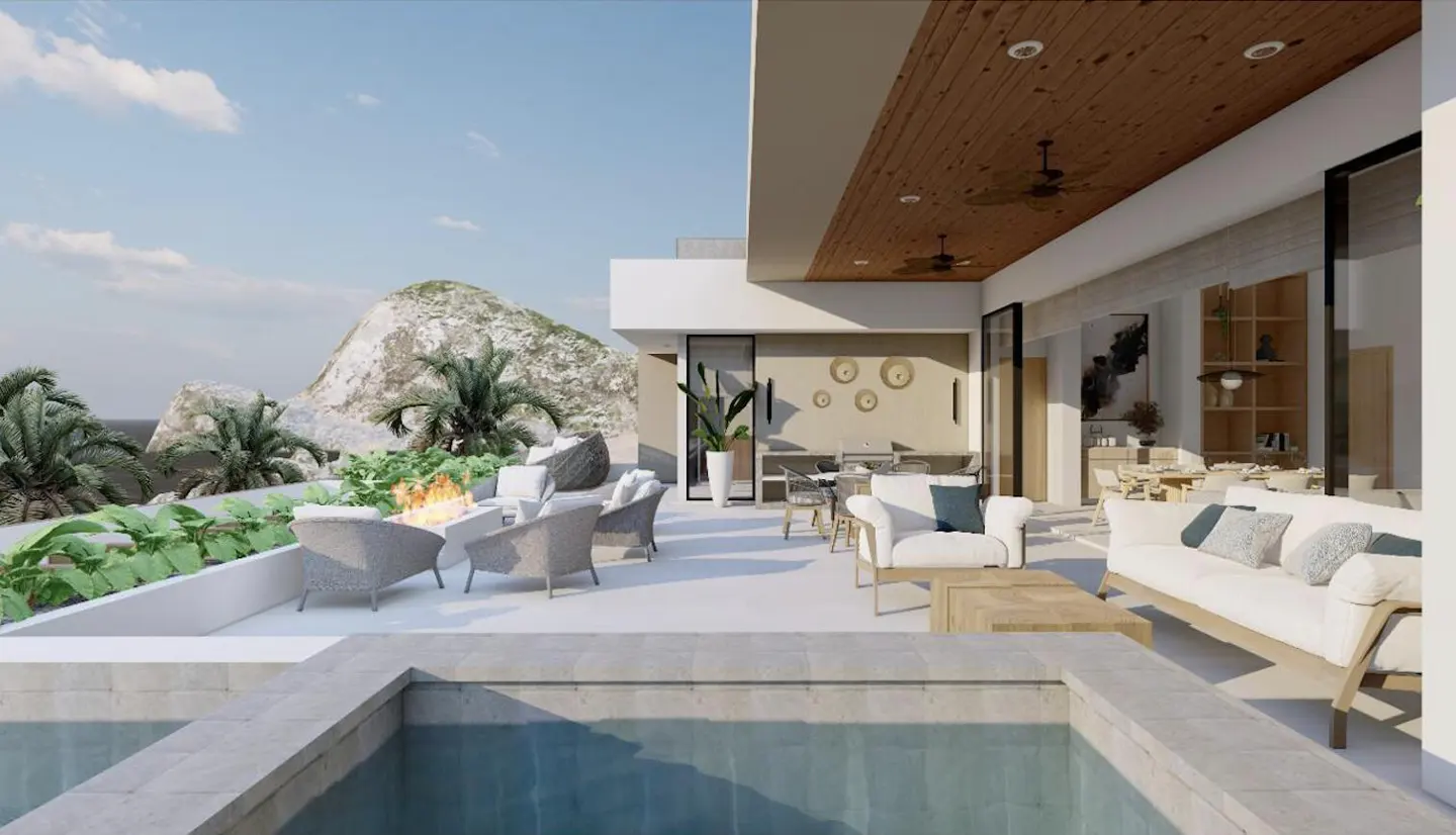 Outdoor patio with a fire pit, wicker chairs, and a view of the ocean and mountains. Inside, there is a dining table and a white sofa.