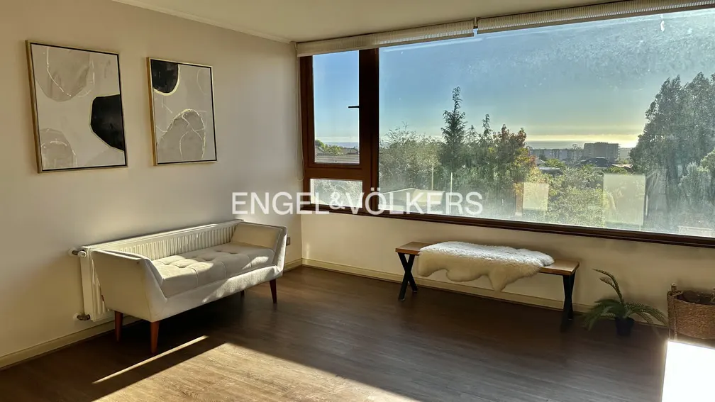 A bright room with a bench, art, and a large window overlooking trees and buildings.