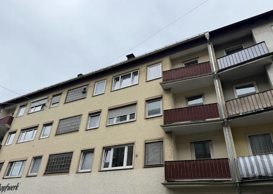 Low angle view of a beige apartment building with brown balconies under a cloudy sky.