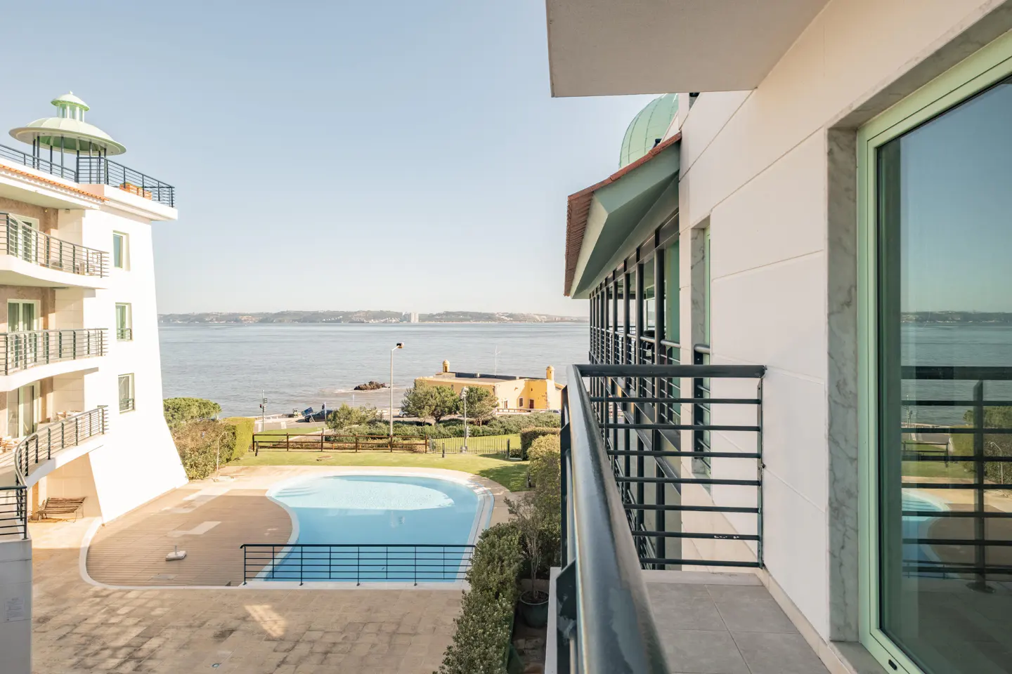 View from a balcony of a white building with a pool and river view.