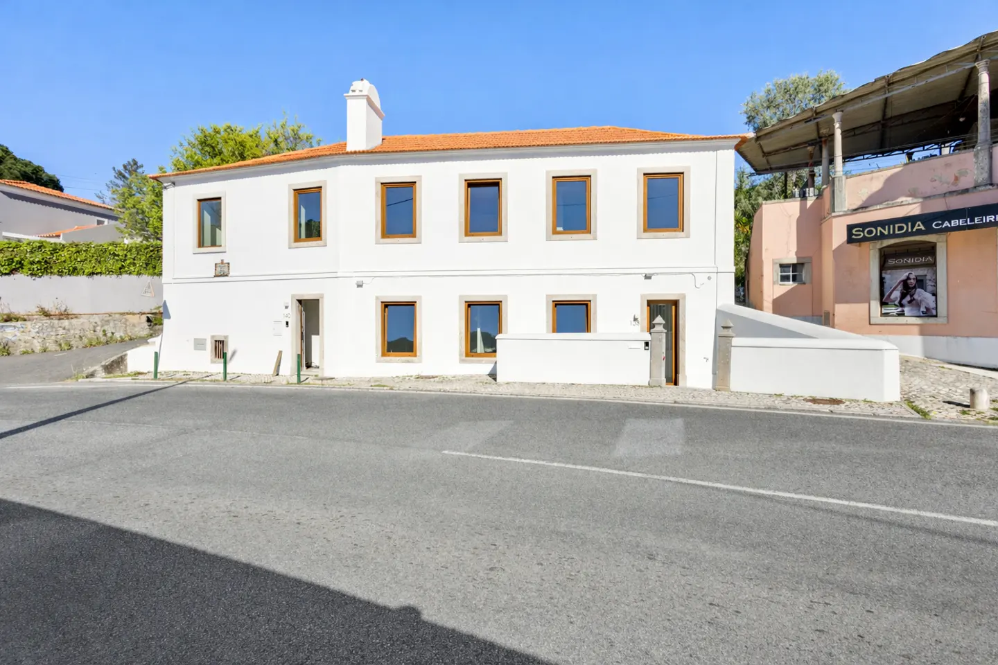 Exterior view of a two-story white house with a red tile roof and brown window frames. A gray road is in the foreground.