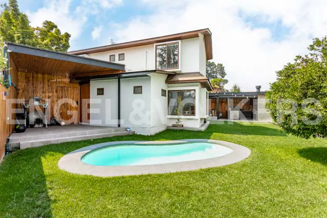 A white two-story house with a turquoise pool and green lawn on a sunny day.