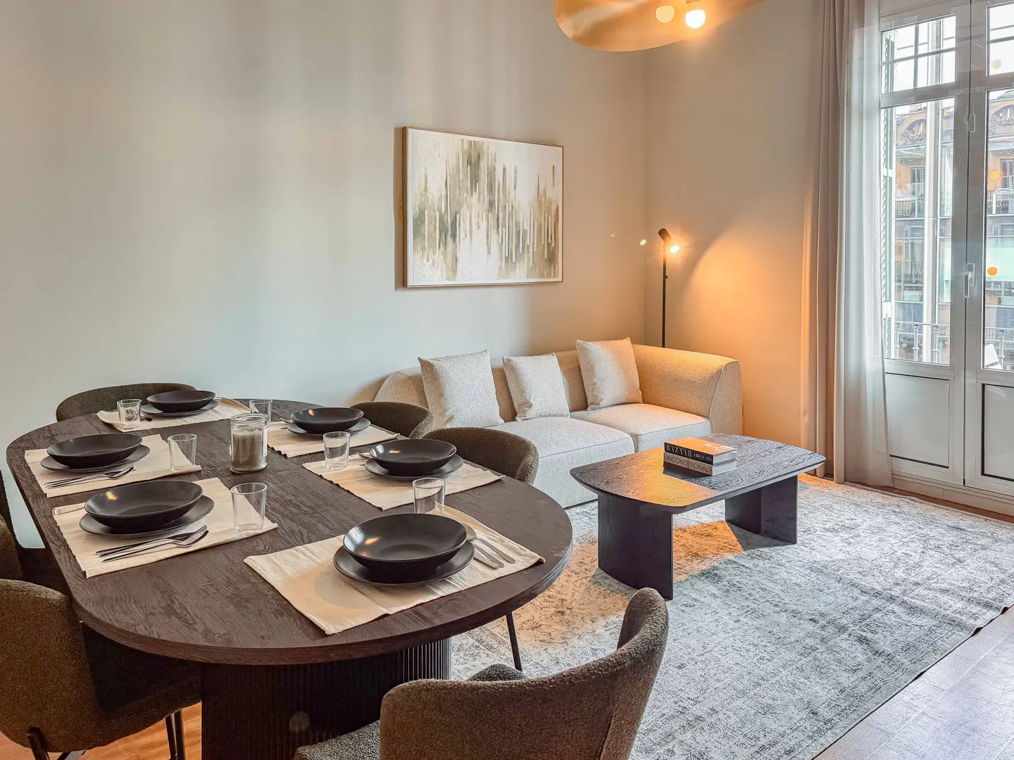 Living room with a dark wood dining table set for six, a beige sofa, and a black coffee table on a gray patterned rug.