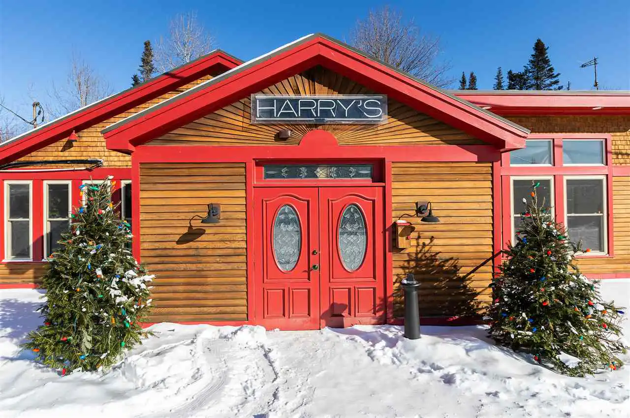 The exterior of Harry's building with red trim, wood siding, and two Christmas trees in the snow.