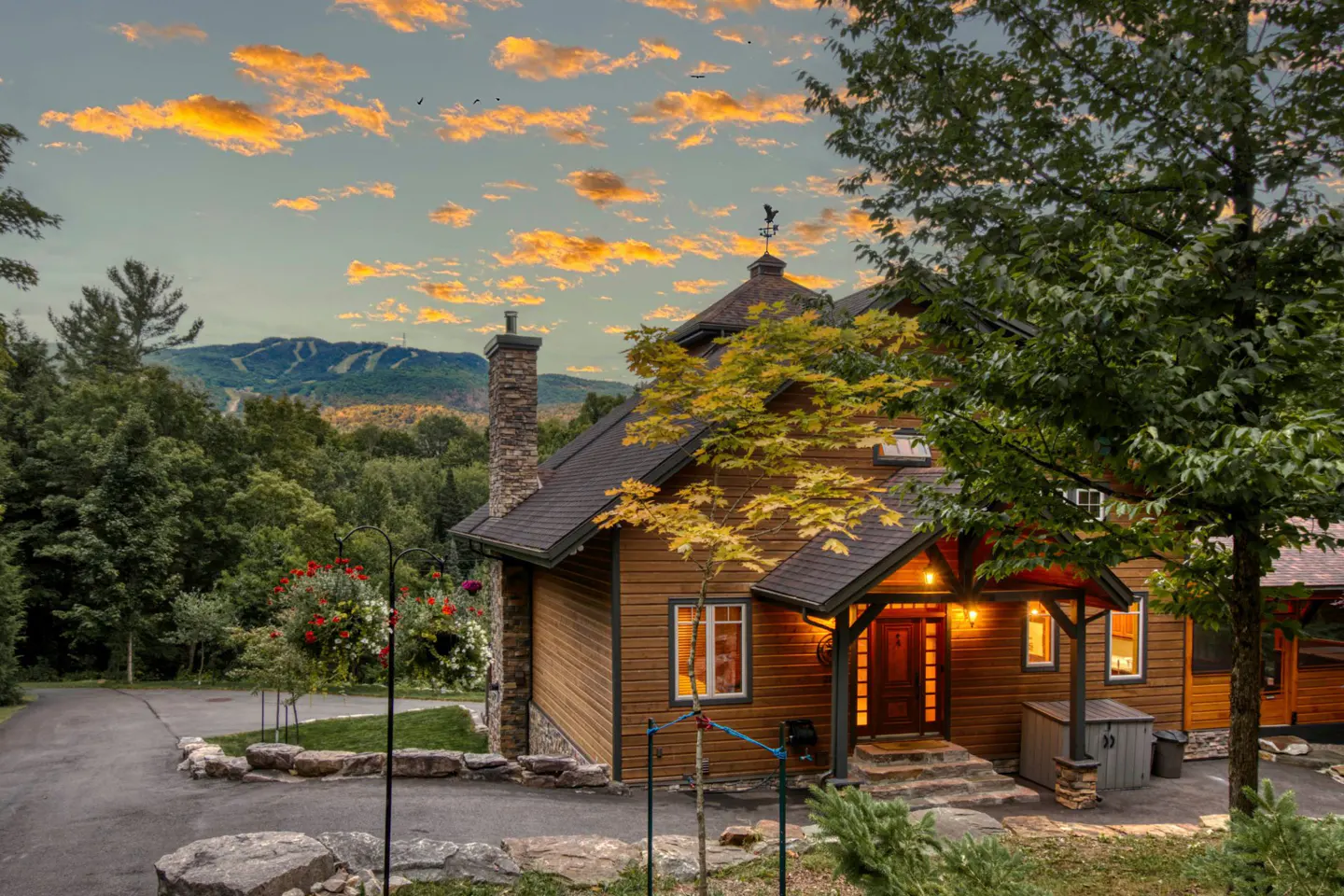 Exterior view of a brown wood house with a stone chimney and a mountain in the background.
