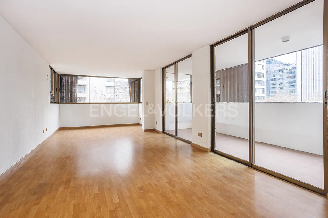 Empty room with light wood floors, white walls, and large sliding glass doors to a balcony with city views.