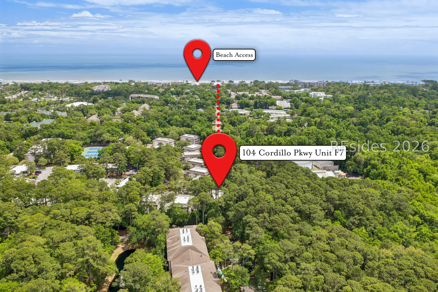 Aerial view of 104 Cordillo Pkwy Unit F7, marked by a red pin, with a dotted line leading to a "Beach Access" pin in the distance. Lush green trees surround the property.