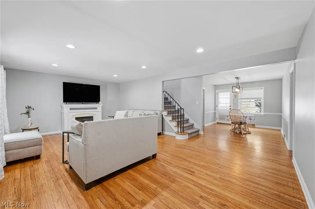 Open-concept living room with hardwood floors, a white fireplace, grey sofa, and stairs leading to a dining area.