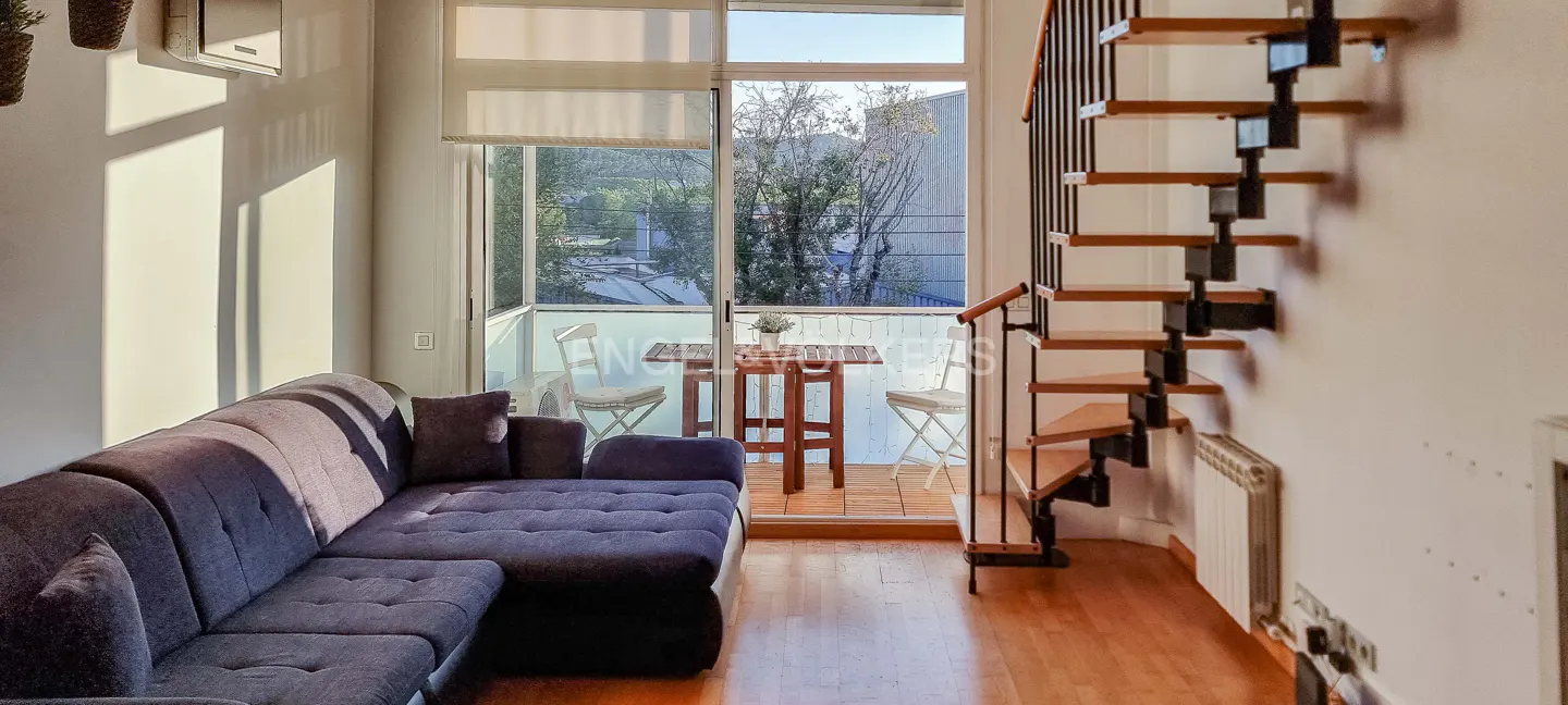 Living room with a blue sofa, wooden stairs, and a balcony with a table and chairs.