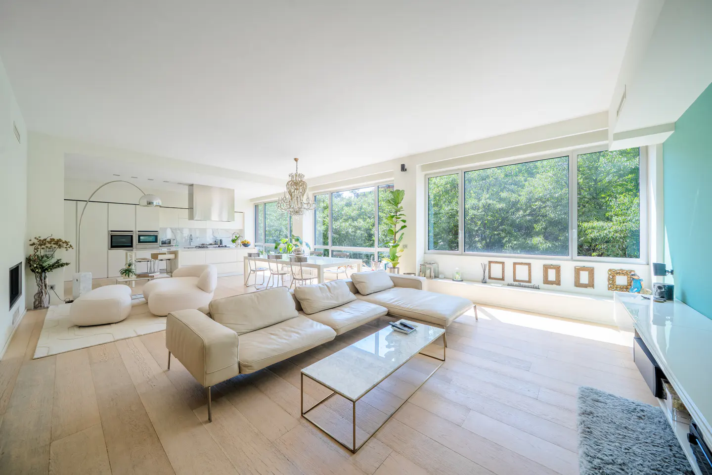 Bright, open-concept living room with a white sectional sofa, glass coffee table, and a modern kitchen in the background.