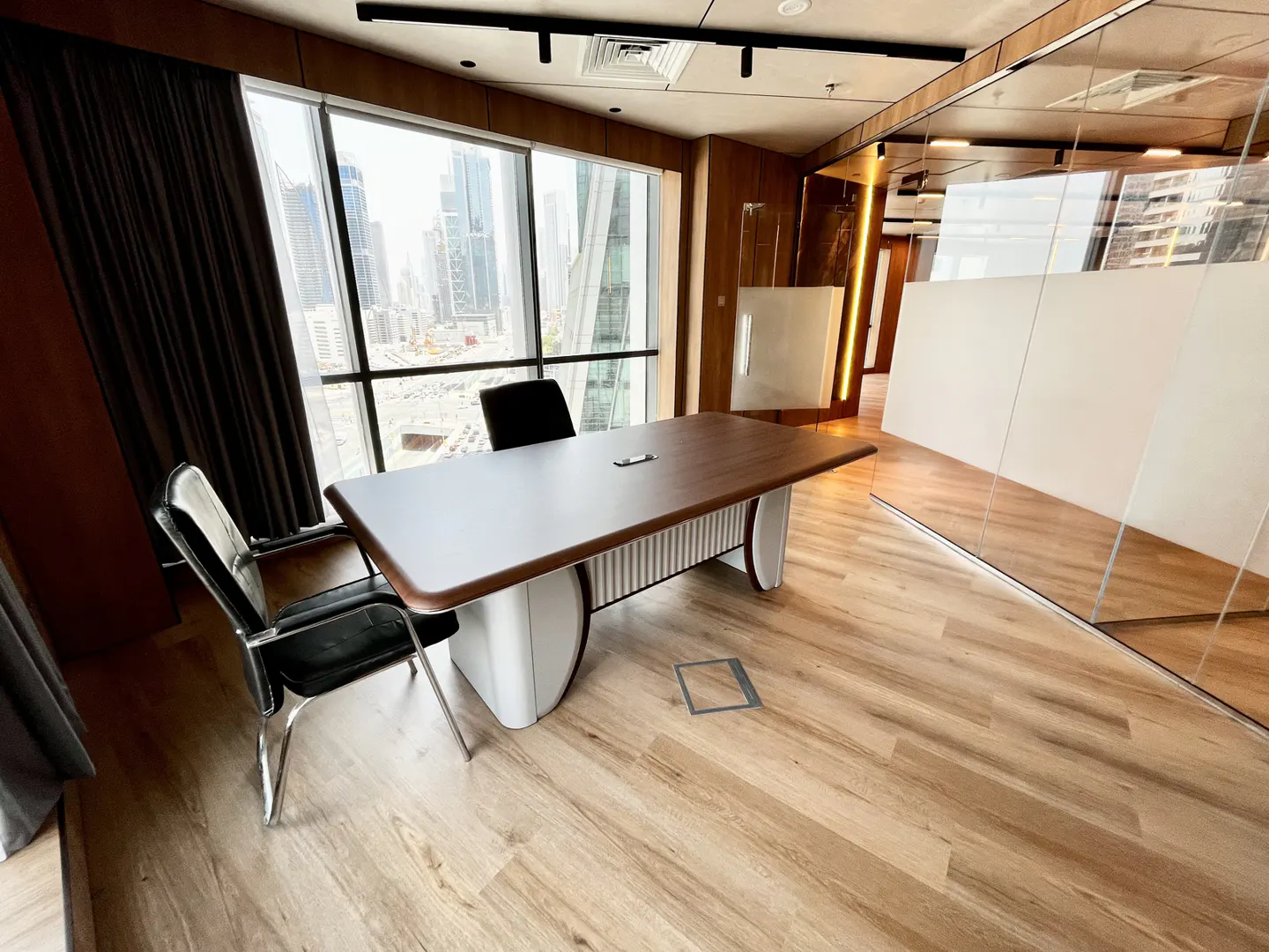 A modern office with a wood desk, black chairs, and a large window overlooking a city skyline.