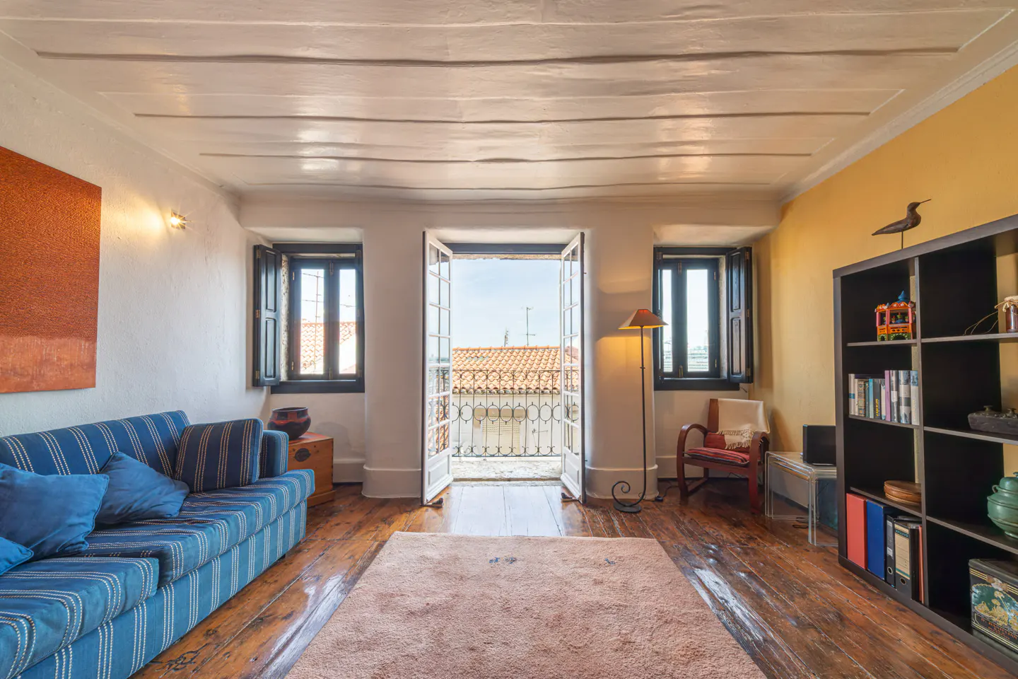 Bright living room with wood floors, a blue striped sofa, and open French doors to a balcony.