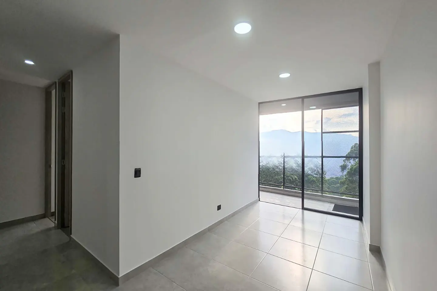 Bright, empty room with white walls, gray tile floor, and sliding glass doors to a balcony with mountain views.
