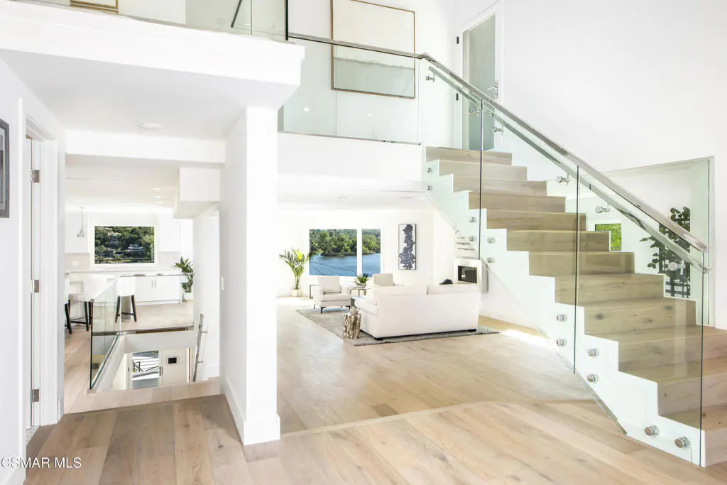 Modern open-concept home interior with light wood floors, a glass-railed staircase, and a bright living area with lake views.